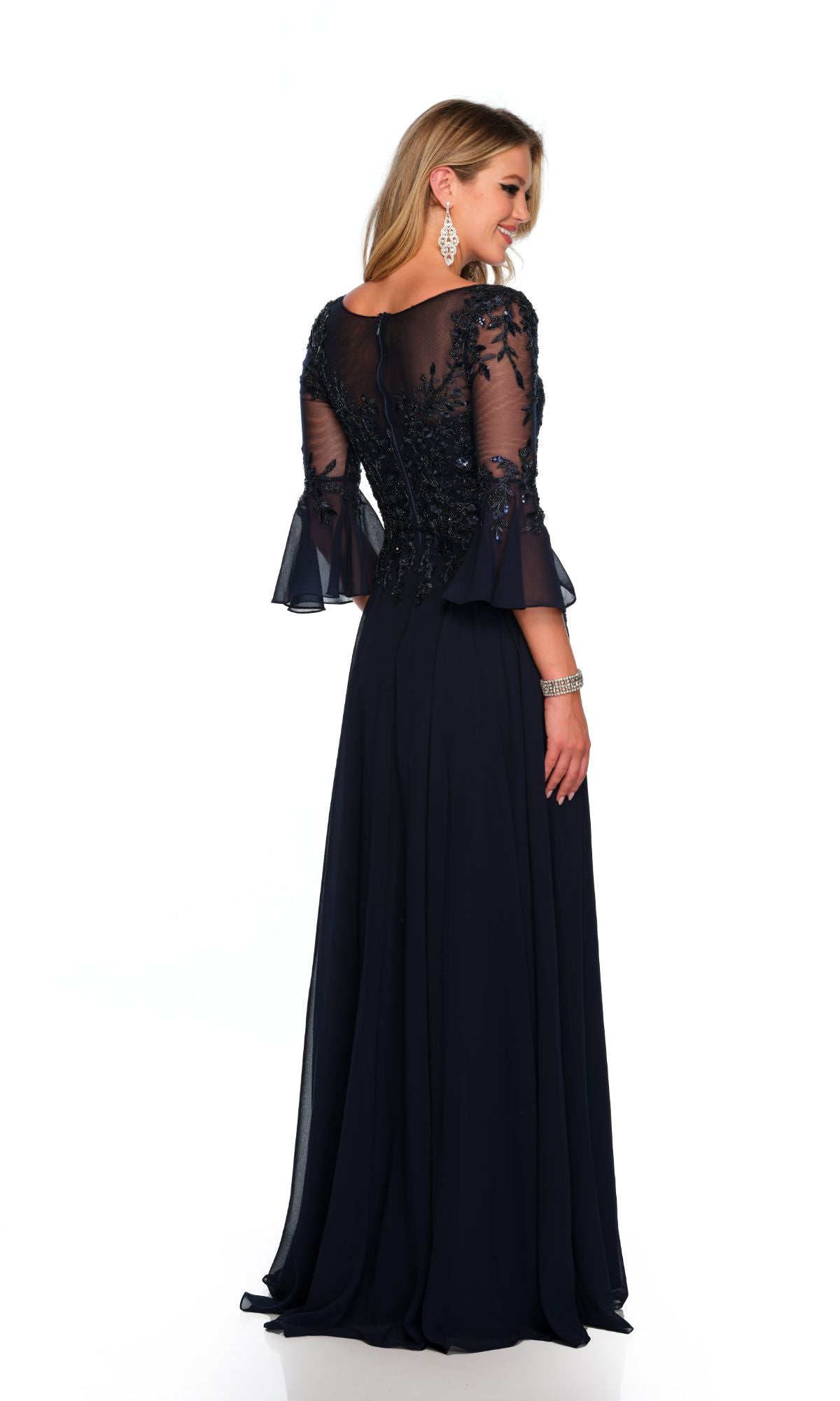 A woman stands against a white background wearing the Long Formal Dress 11602 by Dave and Johnny, a navy blue gown with sheer embroidered sleeves, a fitted bodice, and a subtle v-neckline.